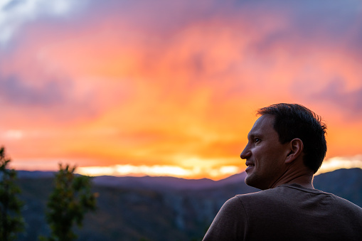 Aspen, Colorado rocky mountains colorful sunset in blurry background with back of young man looking at view at twilight
