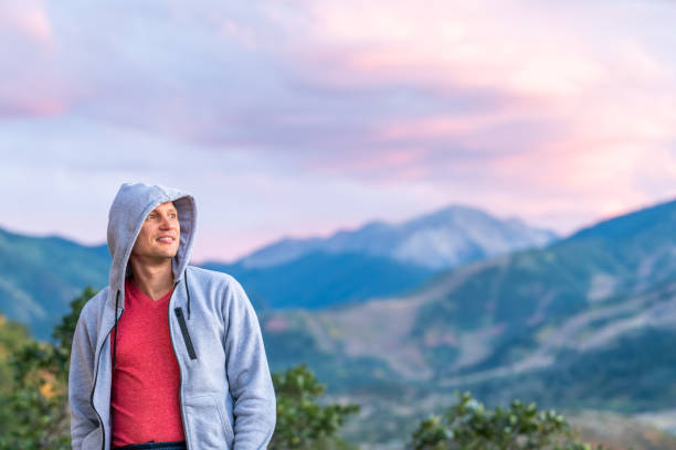 aspen, colorado coloré pourpre crépuscule bleu soleil vertfoncé vue de fond des montagnes rocheuses et jeune homme heureux restant regardant dans le chandail de hoodie - aspen highlands photos et images de collection