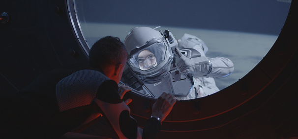 Medium shot of an astronaut talking with his spacewalking crewmate by the spacecraft window