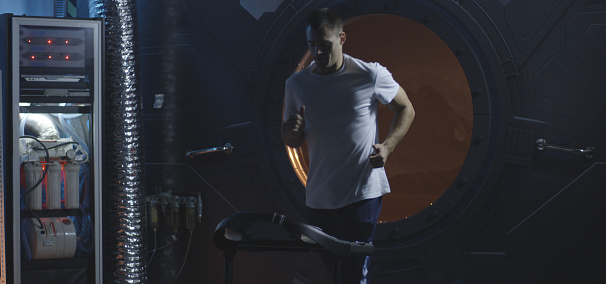 Medium shot of a male astronaut running on a treadmill in a Mars base