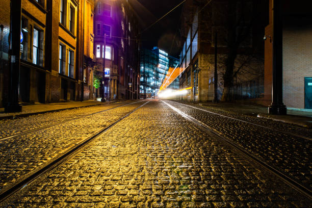 longue exposition d'une rue pavée humide à manchester. traînée l�égère causée par le passage du tram. - night wet road street photos et images de collection