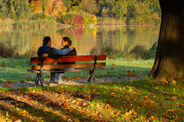 istock Couple sitting on a bench in a public park during Autumn 1190459932