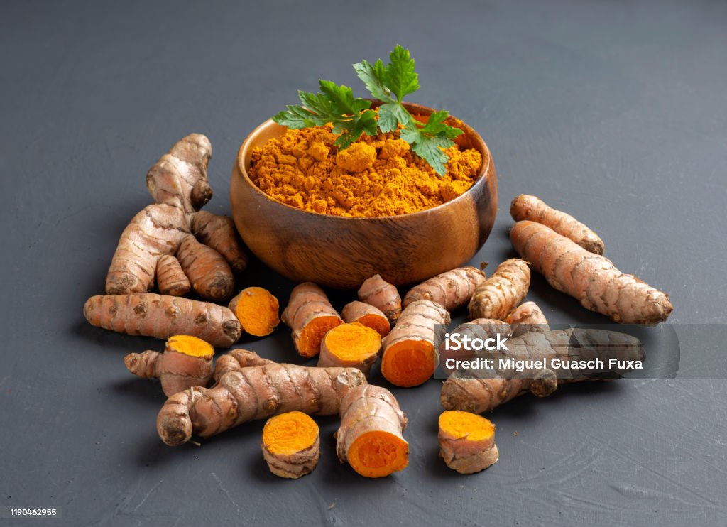 Turmeric powder in a wooden bowl and fresh turmeric Turmeric powder in a wooden bowl and fresh turmeric on dark background Turmeric Stock Photo