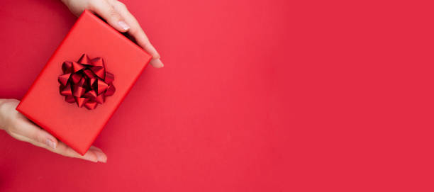 istock Female hands holding gift box with red ribbon bow isolated over flat lay background, copy space. Baner. 1190464708