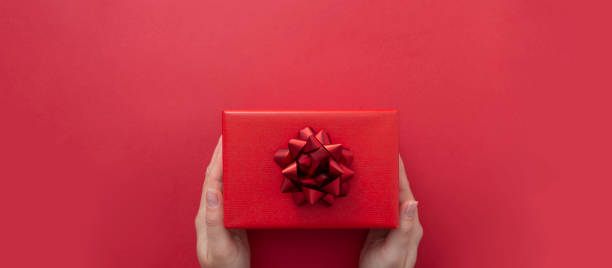 istock Female hands holding gift box with red ribbon bow isolated over flat lay background, copy space. Baner. 1190464745