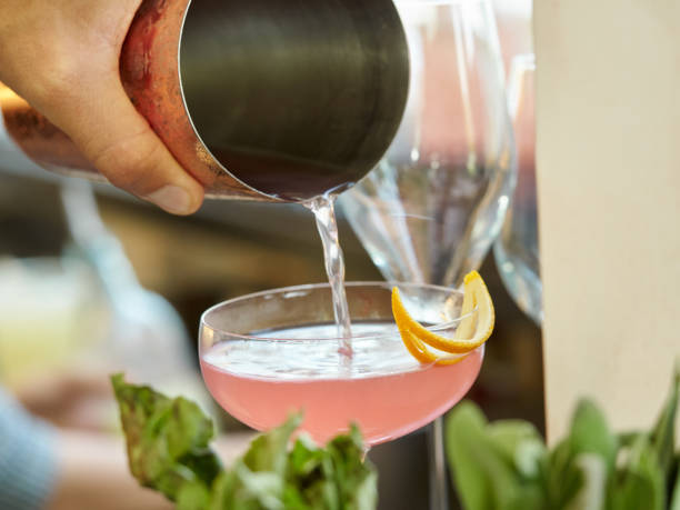 istock Hand holding copper shaker pouring a pink drink into sparkling wine garnished with half moon shaped orange zest 1190489392