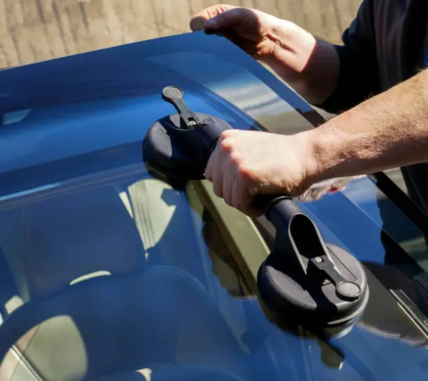 Photo of Automobile special workers replacing windscreen or windshield of a car in front of a building. Background