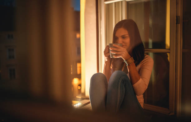 istock Contemplative Young Woman with Tea in Open Window at Dusk 1190505530