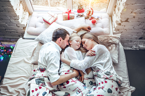Happy family, mother, father and daughter resting on the white bed. Christmas decorations