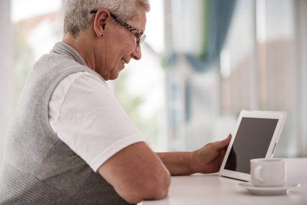 istock Cheerful senior woman enjoying while using her digital tablet 1190505722