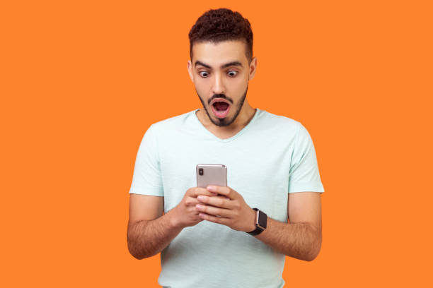 istock Portrait of young brunette man expressing amazement while using cellphone. isolated on orange background 1190506776