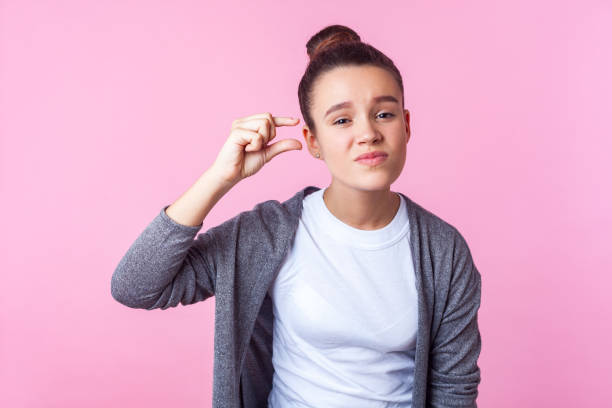 s'll vous plaît, un peu plus. verticale de l'adolescente de brunette bouleversée affichant la petite taille ou le geste peu de peu. fond rose - less fortunate photos et images de collection