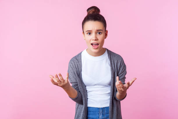 How could you. Portrait of brunette teen girl raising hands asking why, looking indignant displeased. pink background How could you. Portrait of brunette teen girl with bun hairstyle in casual clothes raising hands asking why, looking indignant displeased, making claims. indoor studio shot isolated on pink background sad 15 years old girl stock pictures, royalty-free photos & images
