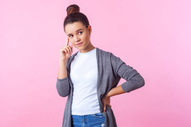 retrato de pensativo linda morena adolescente chica con peinado bollo en ropa casual sosteniendo su cara, pensando con la mano en la cintura y mirando hacia otro lado. - teenager adolescence portrait pensive fotografías e imágenes de stock