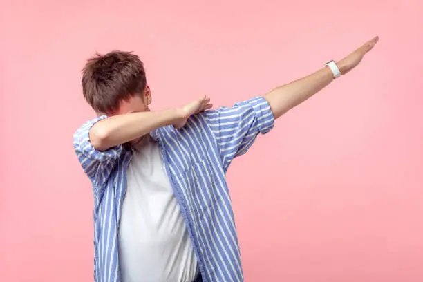Photo of Portrait of anonymous brown-haired man standing in dab dance pose. indoor studio shot isolated on pink background