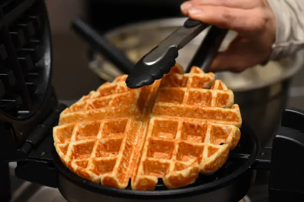 Whole wheat waffle picked out of waffle iron with tongs