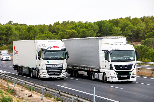 Occitanie, France - September 10, 2019: White semi-trailer trucks DAF XF and MAN TGX at the interurban road.