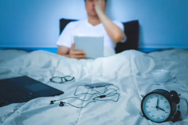 sleepless, headache, tense young asian man working on tablet pc, laptop computer and smartphone in bed at night