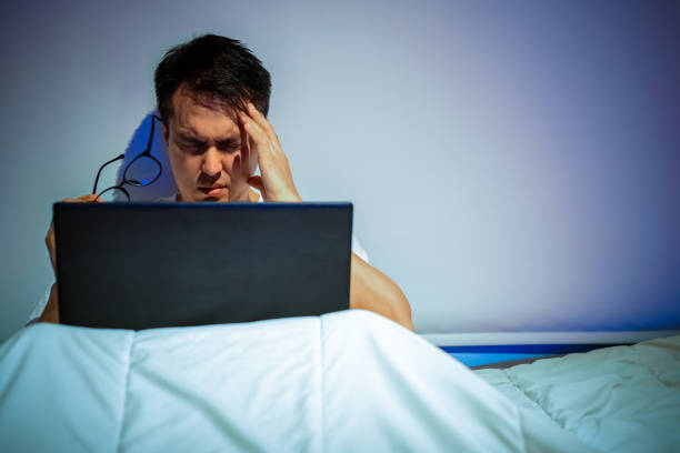 istock headache, tense young asian man working on laptop computer in bed at night 1190546807