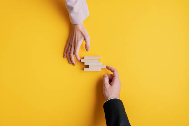 Conceptual image of business stability and teamwork Hands of a businessman and businesswoman stacking wooden pegs in a conceptual image of business stability and teamwork. coalition photos stock pictures, royalty-free photos & images