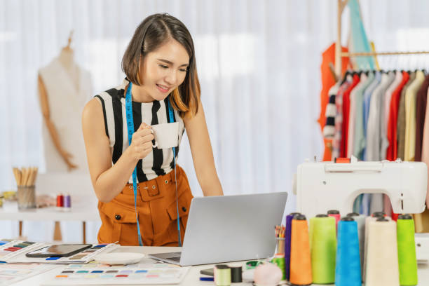 職場でコンピュータのラップトップと多色チャートで働くアジアのデザイナーの女性 - mannequin dressmakers model tape measure textile ストックフォトと画像