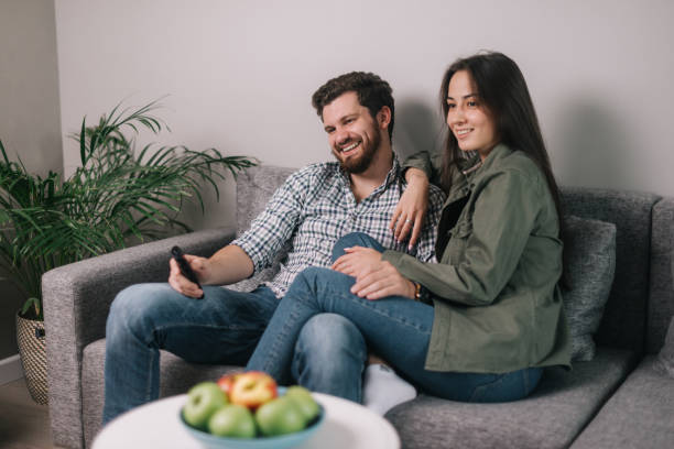 lovely happy couple is watching tv at home sitting on soft sofa. - apartment television family couple imagens e fotografias de stock
