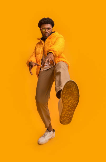 Black funny guy showing beast, stepping on camera Black funny guy in winter jacket showing beast, stepping on camera, orange background fool photos stock pictures, royalty-free photos & images