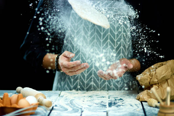 istock The man, chef cooks throws the dough, flying, freezing in motion. On a black background. White flour flying into air. Hands preparing dough 1190572571