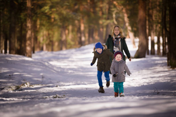 happy children with mom run through the snowy winter forest. cute cheerful family is walking in the park on a sunny cold day. - family winter walking fun imagens e fotografias de stock