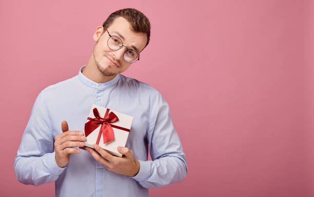 istock Man in shirt holds gift in box, looking straight 1190574285