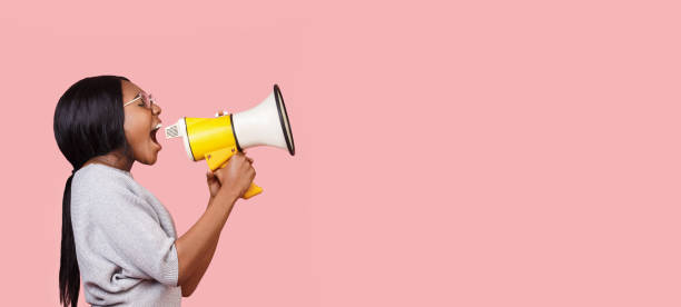 istock Young woman shouting in megaphone over pink background 1190575428