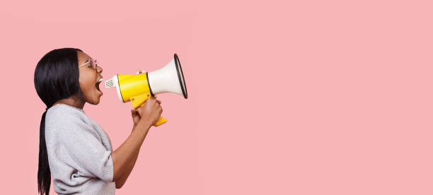 Young woman shouting in megaphone over pink background Making announcement. Black woman shouting in megaphone towards copy space over pink background, panorama mouth photos stock pictures, royalty-free photos & images