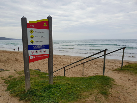 Vertical closeup photo of colorful information signs on a metal pole in a grass area next to a pathway leading down to the sand at popular travel destination, Wategos Beach, subtropical north coast NSW. 9th August, 2023.