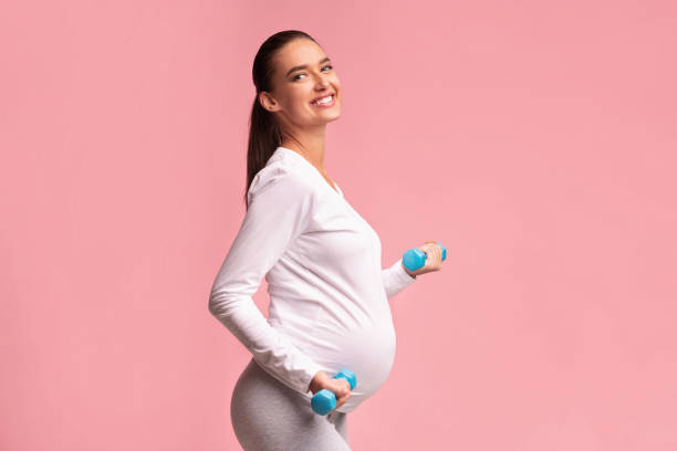 mujer expectante positiva haciendo ejercicio con dumbbells de pie en el estudio - relaxation exercise child mother human pregnancy fotografías e imágenes de stock