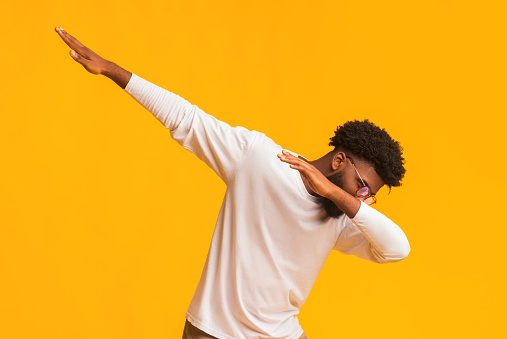 African american man throwing dab move, dancing against orange studio background, copy space