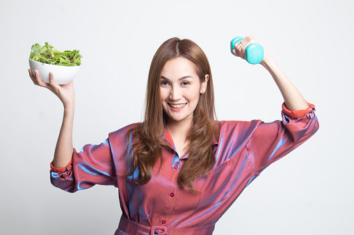 Healthy Asian woman with dumbbells and salad on white background