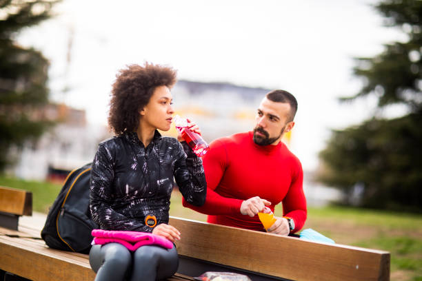 istock Young athletic couple drinking energy drinks together while sitting on a park bench 1190578484