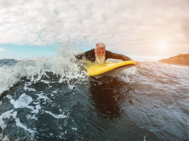 istock Senior man doing surf with longboard riding a wave - Happy old guy having fun doing extreme sport - Joyful elderly concept - Focus on his face 1190582262