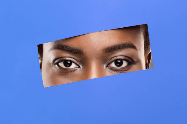 istock Afro woman's eyes without makeup peeking from hole in blue paper 1190582274