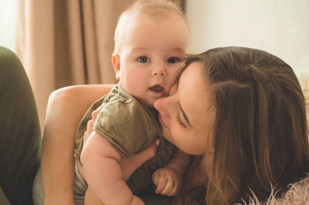 Home portrait of a baby boy with mother on the bed. Mom holding and kissing her child. Home portrait of a baby boy with mother on the bed. Mom holding and kissing her child. Mother day concept cute boy show love symbol hand stock pictures, royalty-free photos & images