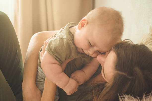 Home portrait of a baby boy with mother on the bed. Mom holding and kissing her child. Home portrait of a baby boy with mother on the bed. Mom holding and kissing her child. Mother day concept cute boy show love symbol hand stock pictures, royalty-free photos & images