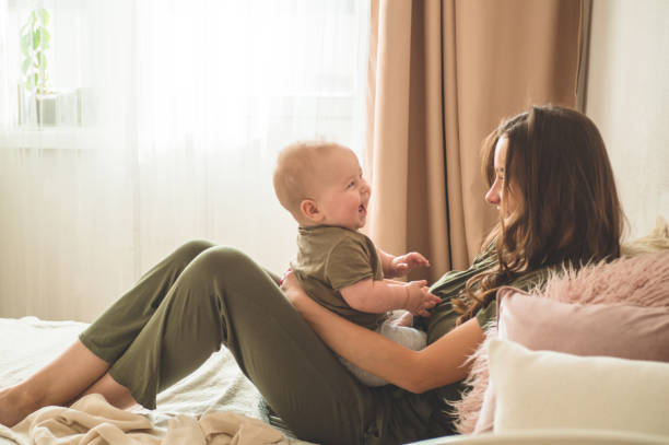 Home portrait of a baby boy with mother on the bed. Mom holding and kissing her child. Home portrait of a baby boy with mother on the bed. Mom holding and kissing her child. Mother day concept cute boy show love symbol hand stock pictures, royalty-free photos & images
