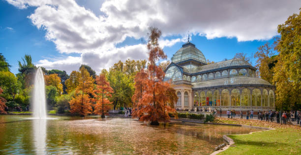 Crystal palace in Retiro at autumn Park, Madrid November 3, 2019 - Madrid, Spain: Tourists and locals gather outside the Crystal Palace (Palacio de Cristal) in the Retiro Park in Madrid at autumn. Designed by architect Ricardo Velázquez Bosco, it was built in 1887 to exhibit flora and fauna from the Philippines palacio de cristal photos stock pictures, royalty-free photos & images