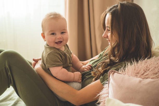 Home portrait of a baby boy with mother on the bed. Mom holding and kissing her child. Home portrait of a baby boy with mother on the bed. Mom holding and kissing her child. Mother day concept cute boy show love symbol hand stock pictures, royalty-free photos & images