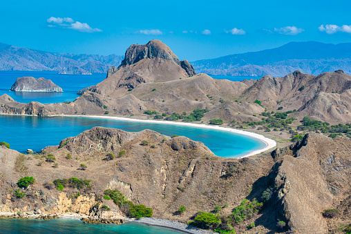 Aerial shot of the mountains and bays of Padar island (Pulau Padar) in the Komodo National Park, Lesser Sunda Islands, Indonesia. In the background the island Komodo is visible, this is the home of the Komodo Dragon (Varanus komodoensis), the largest living species of lizard, growing to a maximum length of 3 meters.