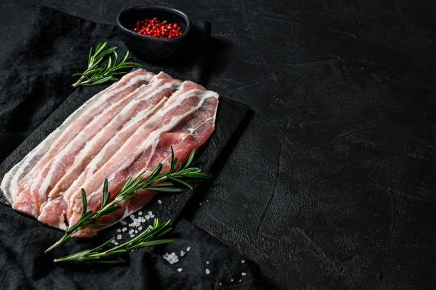 istock Raw bacon on a stone chopping Board. Pork meat. Black background. Top view. Space for text 1190598252