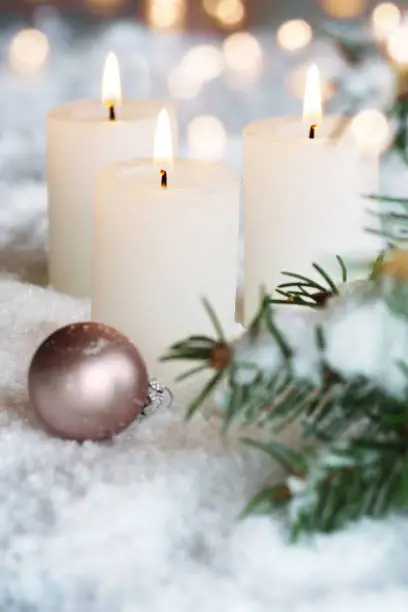 Three white advent candles decorated in snow with festive golden bokeh