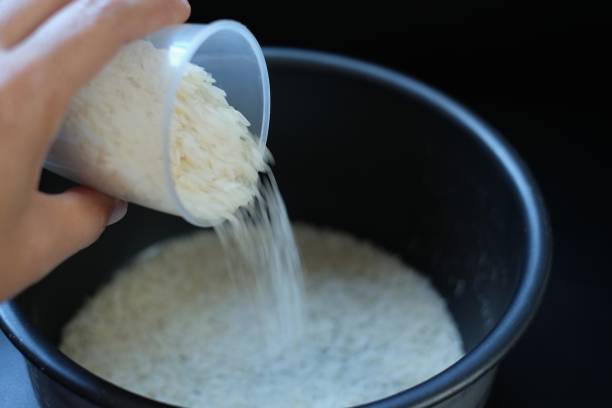 istock Rice flows from glass into rice cooker on black background 1190607209