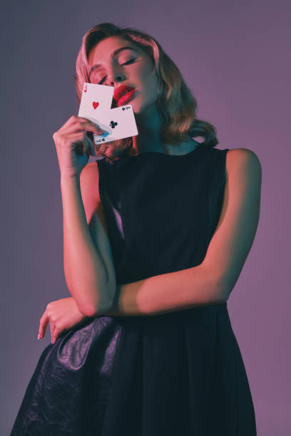 blondynka w czarnej stylowej sukience pokazująca dwie karty do gry, pozując na kolorowym tle. rozrywka hazardowa, poker, kasyno. zbliżenie - casino black and white gambling chip gambling zdjęcia i obrazy z banku zdjęć