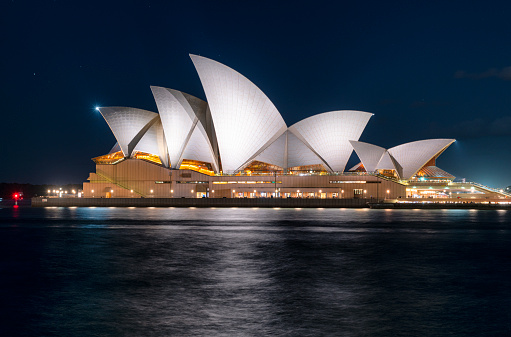 Sydney Australia - August 19, 2019: Night-time in Sydney, and the brightly-illuminated shape of the city's Opera House seems to glow in the darkness.